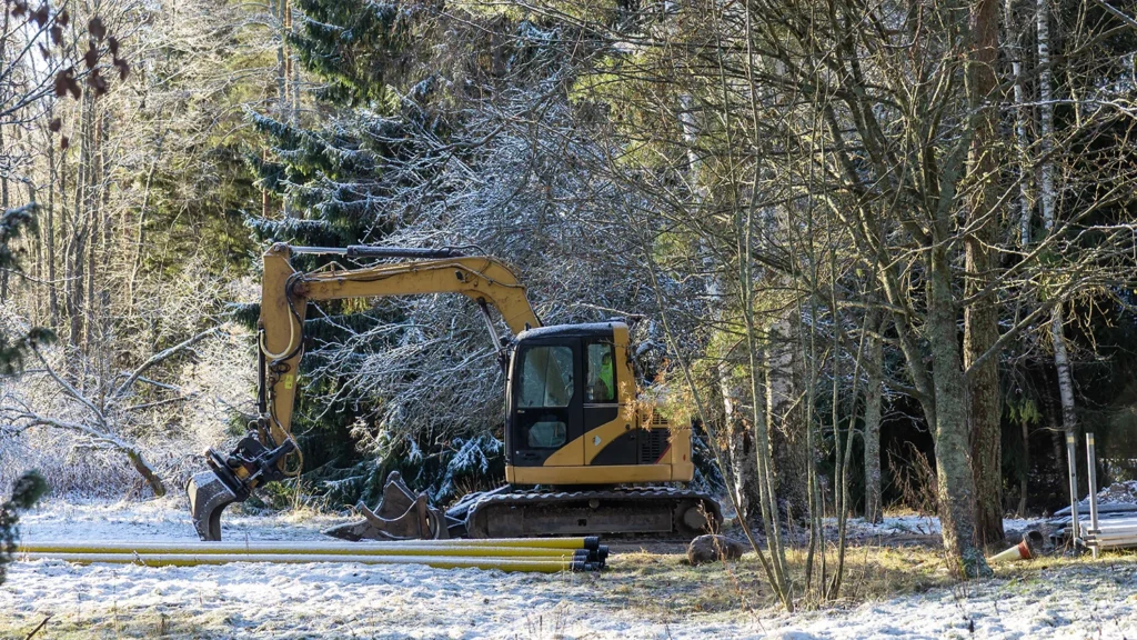 An excavator stands idle on a snow-covered construction site, surrounded by winter conditions and a quiet, frozen landscape
