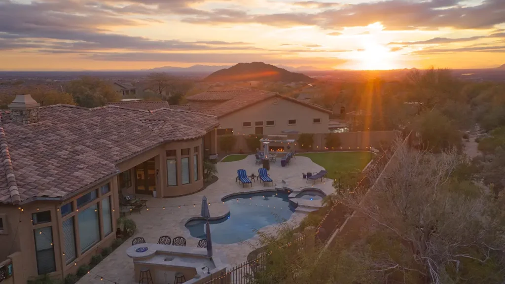 A landscaped backyard featuring a travertine tile pool deck, fireplace and outdoor kitchen.