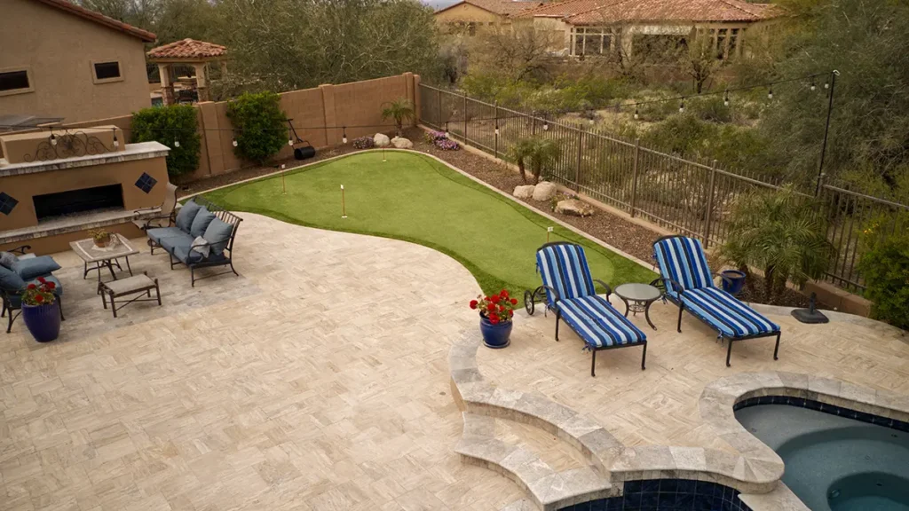 An artificial grass putting green in a desert landscaped backyard with a pool and outdoor seating areas