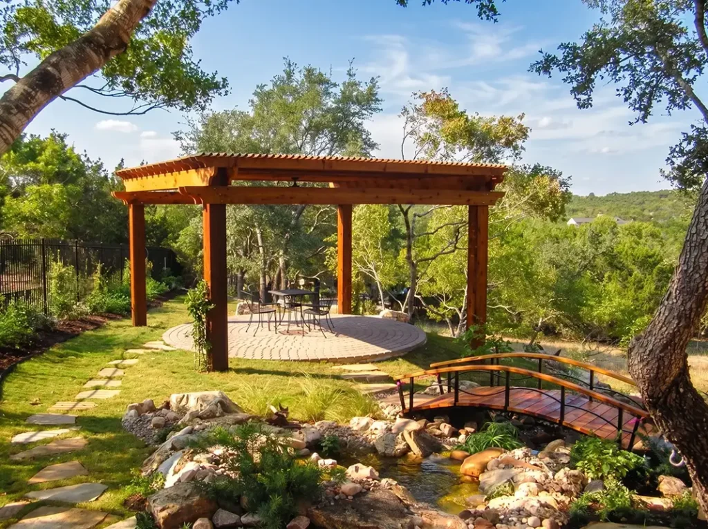 a pergola sits next to a bridge over a dry creek bed