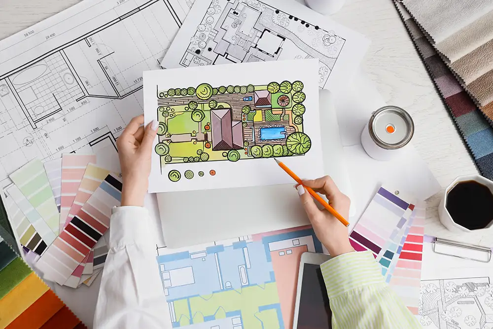 Landscape architect designing residential garden plan with color palette and blueprints on white desk