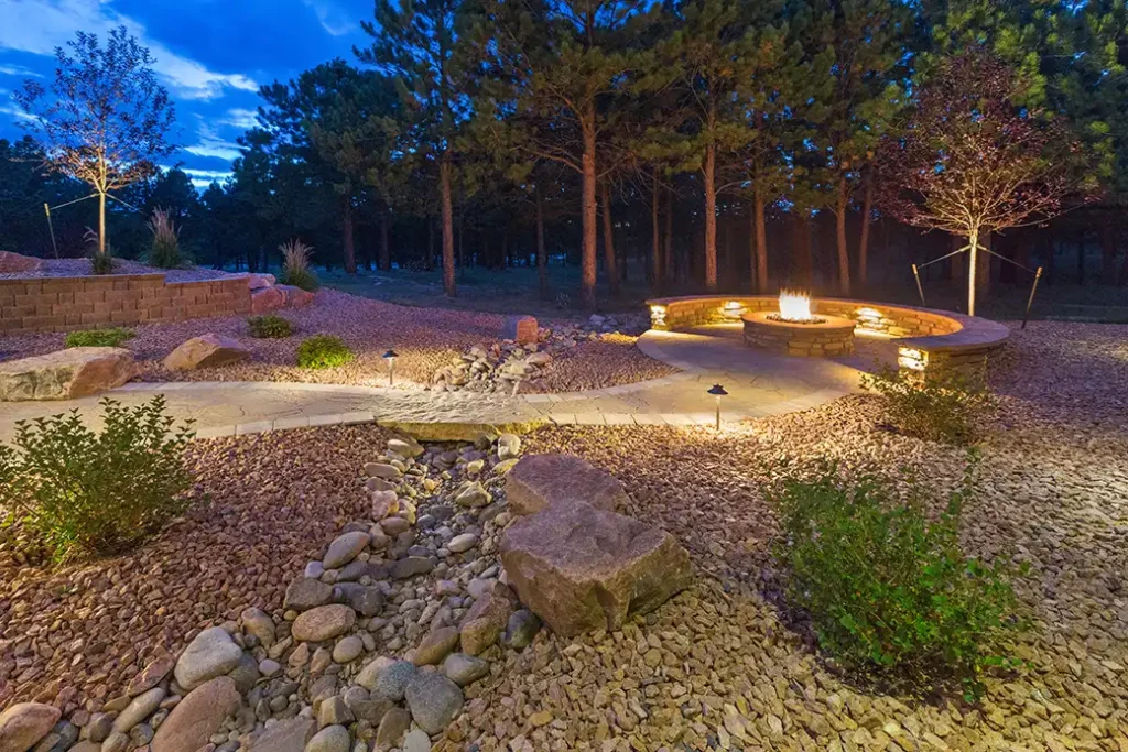 Outdoor living space with gravel, large rocks, bushes, stone seating, and fire pit