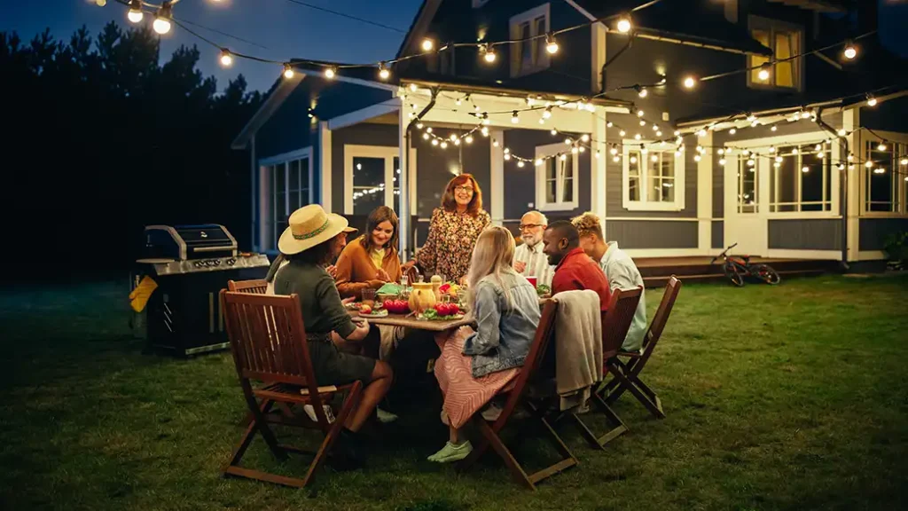 Friends Gathered at a Barbecue Dinner Table Outside a Beautiful Home with outdoor lighting